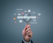 a man's hand holds a magnifying glass up to the graphic of a website search bar