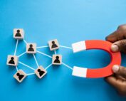 A person holding a red and grey magnet connceted to blocks with icons of people on them representing lead generation