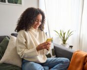 Happy young woman sitting on sofa holding mobile phone.