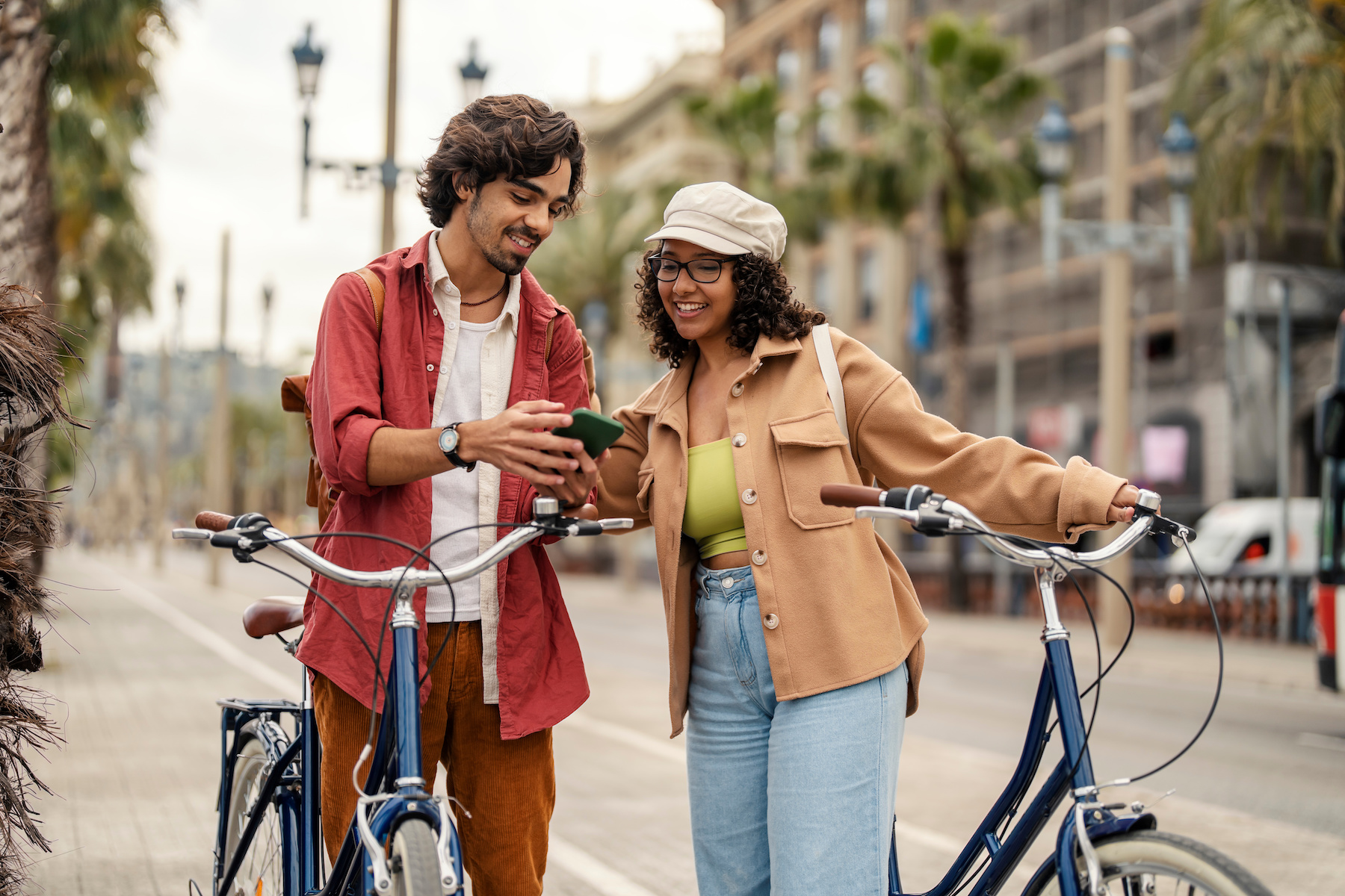 Woman and man standing in street holding their bikes and both looking at phone smiling.