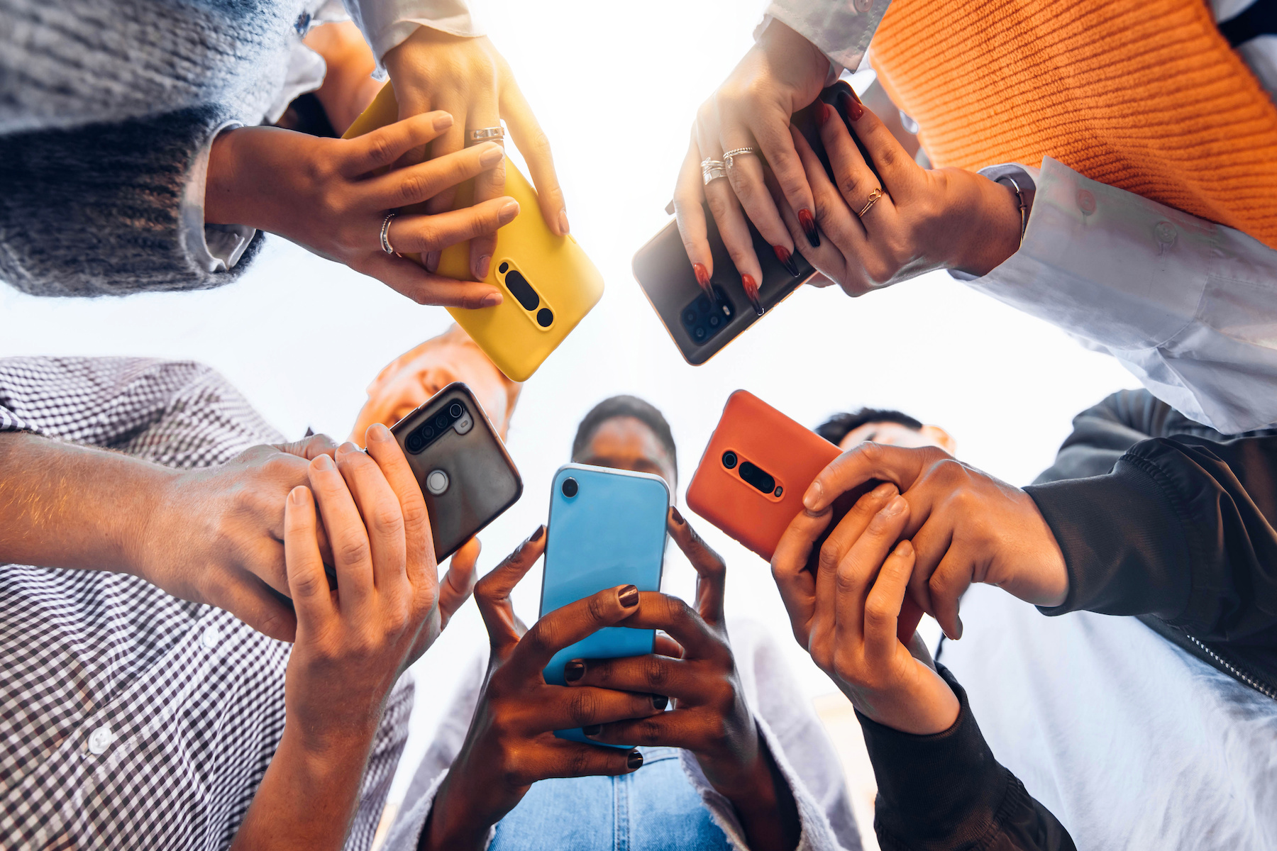 Teens in circle holding smart mobile phones - Multicultural young people using cellphones outside.