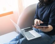 Person using computer and phone sitting on couch.