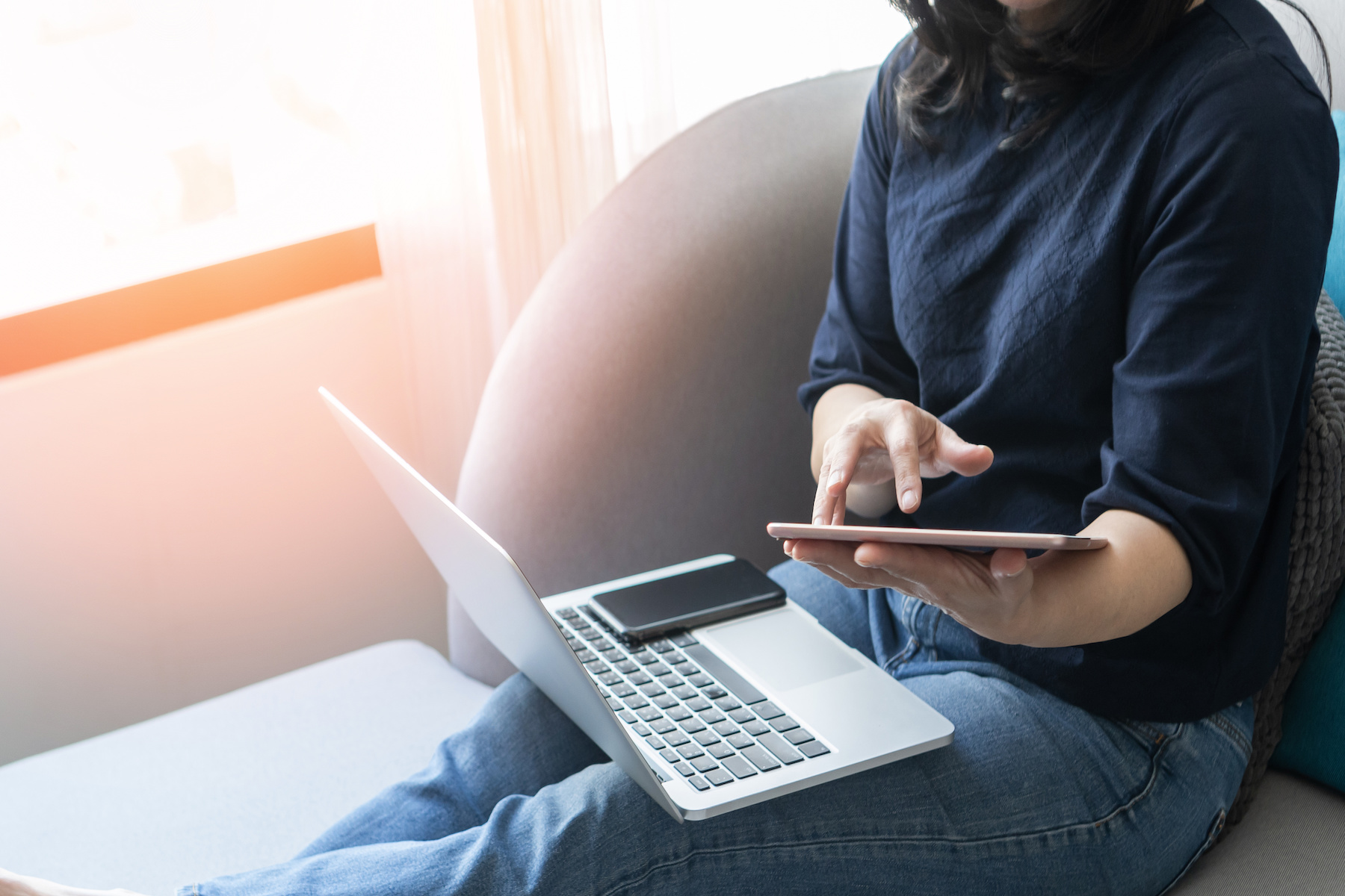Person using computer and phone sitting on couch.