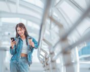 Happy young asian woman using social media on mobile phone while holding coffee cup in a urban city.