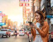 Young asian woman in the city, using phone and smiling.