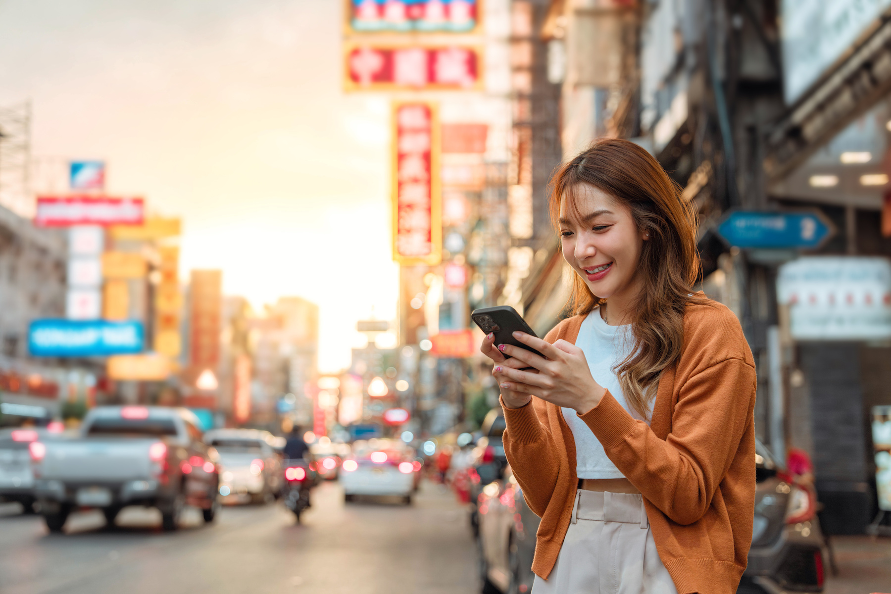 Young asian woman in the city, using phone and smiling.