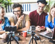 Group of peoplelaughing sitting on table recording video of themselves.