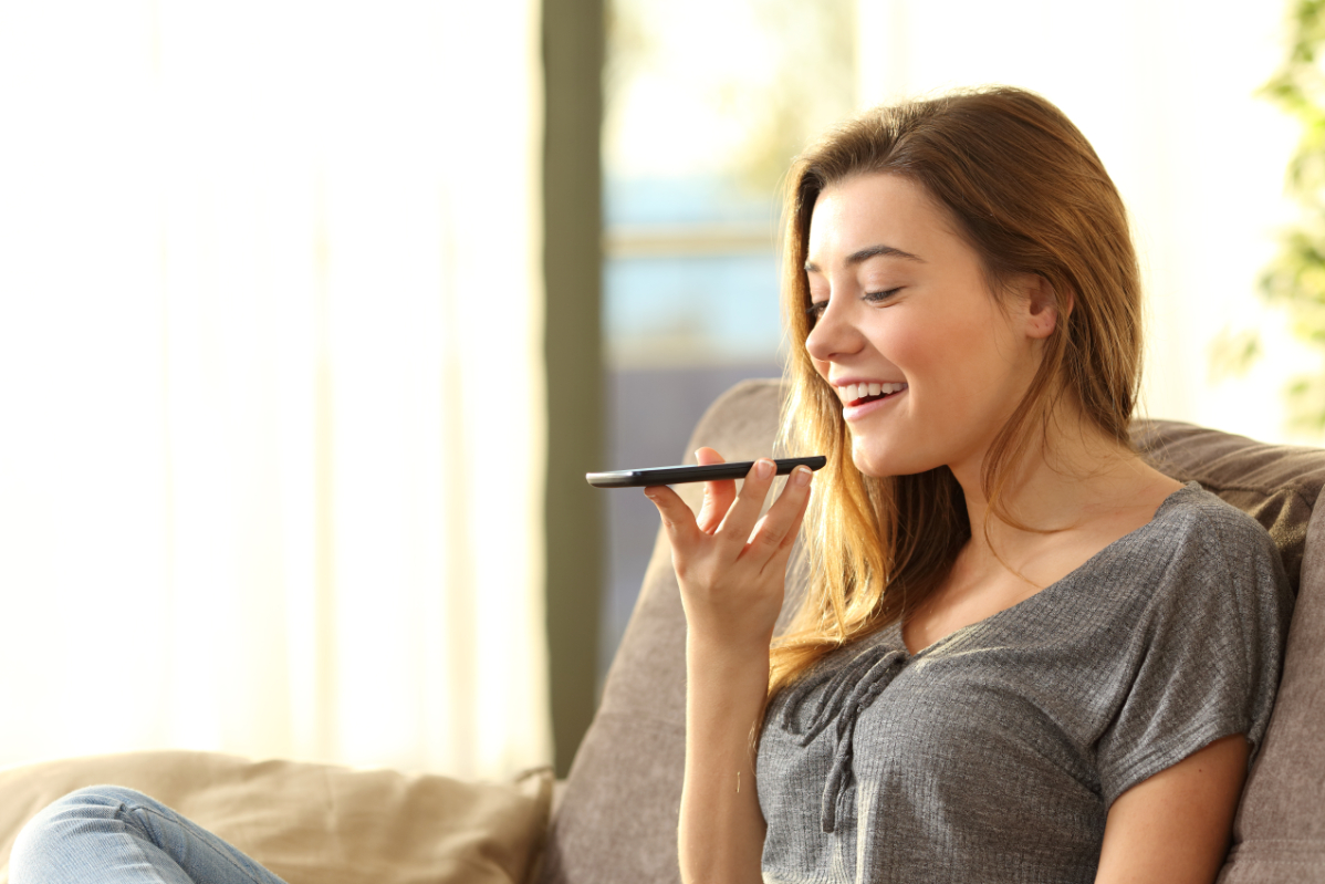 Woman sitting on couch and using voice search on phone.