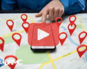 Top view of map with red location designs over it and phone placed on the middle displaying map on screen. Person touching screen. Red play button on the center of image.