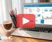 A laptop screen displaying website traffic analytics, with charts and metrics showing user engagement and data trends. A cup of coffee and colorful pencils add a workspace feel.