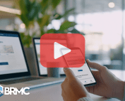 Person holding phone. Laptops on the background. Red play design and BRMC logo.