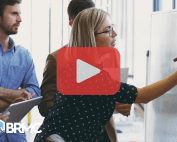 A team collaborating at a whiteboard, with a play button overlay, suggesting a training or strategy video.