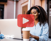 Woman working on laptop with coffee next to her. Red play buttom overlay and BRMC logo.