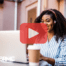 Woman working on laptop with coffee next to her. Red play buttom overlay and BRMC logo.