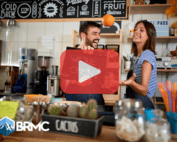 Small business owners in cofee shop. Red play buttom overlay and BRMC logo.